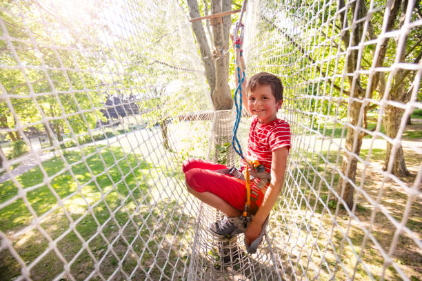 Fun at rope park - little boy smiling portrait in high net between trees